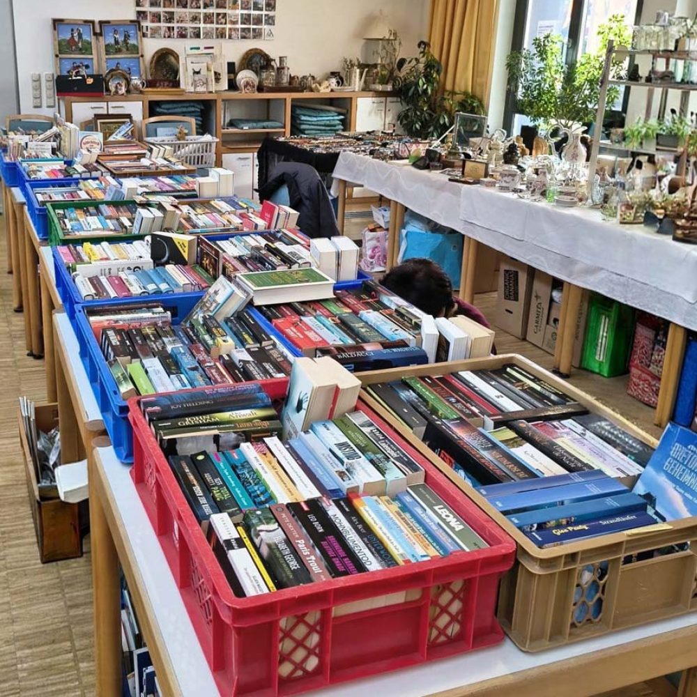 Tische, auf denen Kisten mit Büchern und allerlei Gegenständen wie Keramik, Schmuck und gerahmten Fotos stehen. Ganz im Stil eines Münchner Flohmarkts, um Spenden für den Tierschutz zu sammeln.